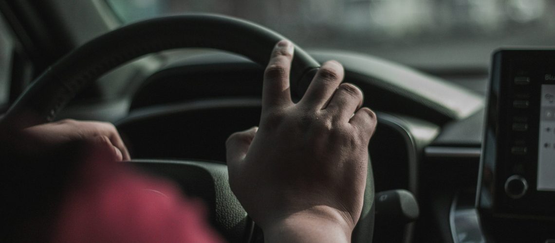 An individual gripping a steering wheel, signaling a car accident on the roadway and responsibility for an insurance claim.